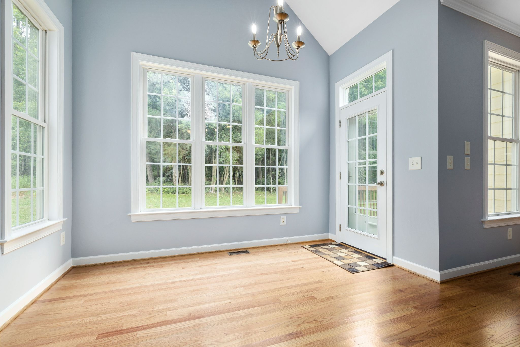 Home interior with large windows on each blue-painted wall in the background and vinyl floor-planks shining in the sun in foreground
