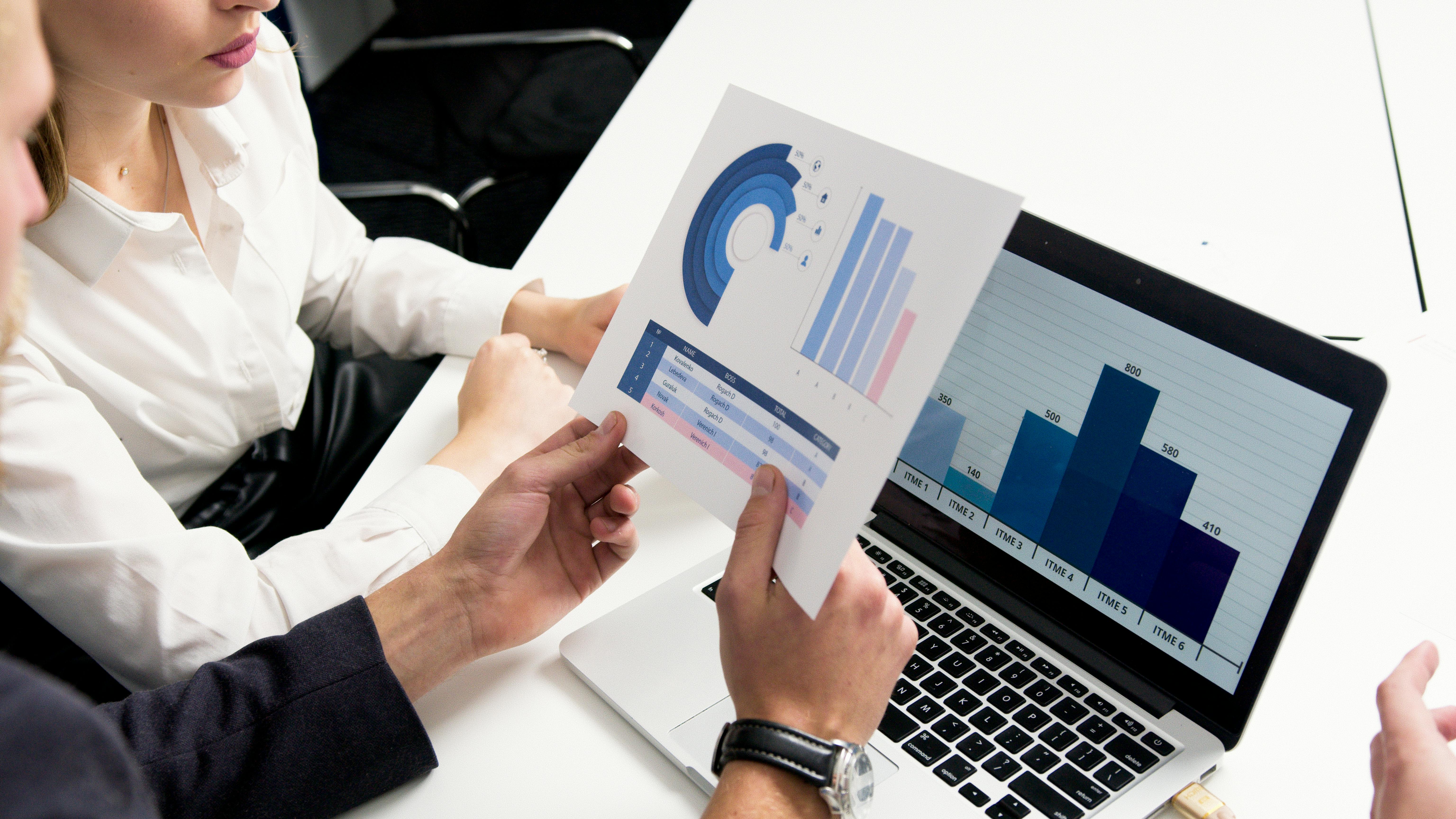 two people looking at papers and computer screens with graphs on them