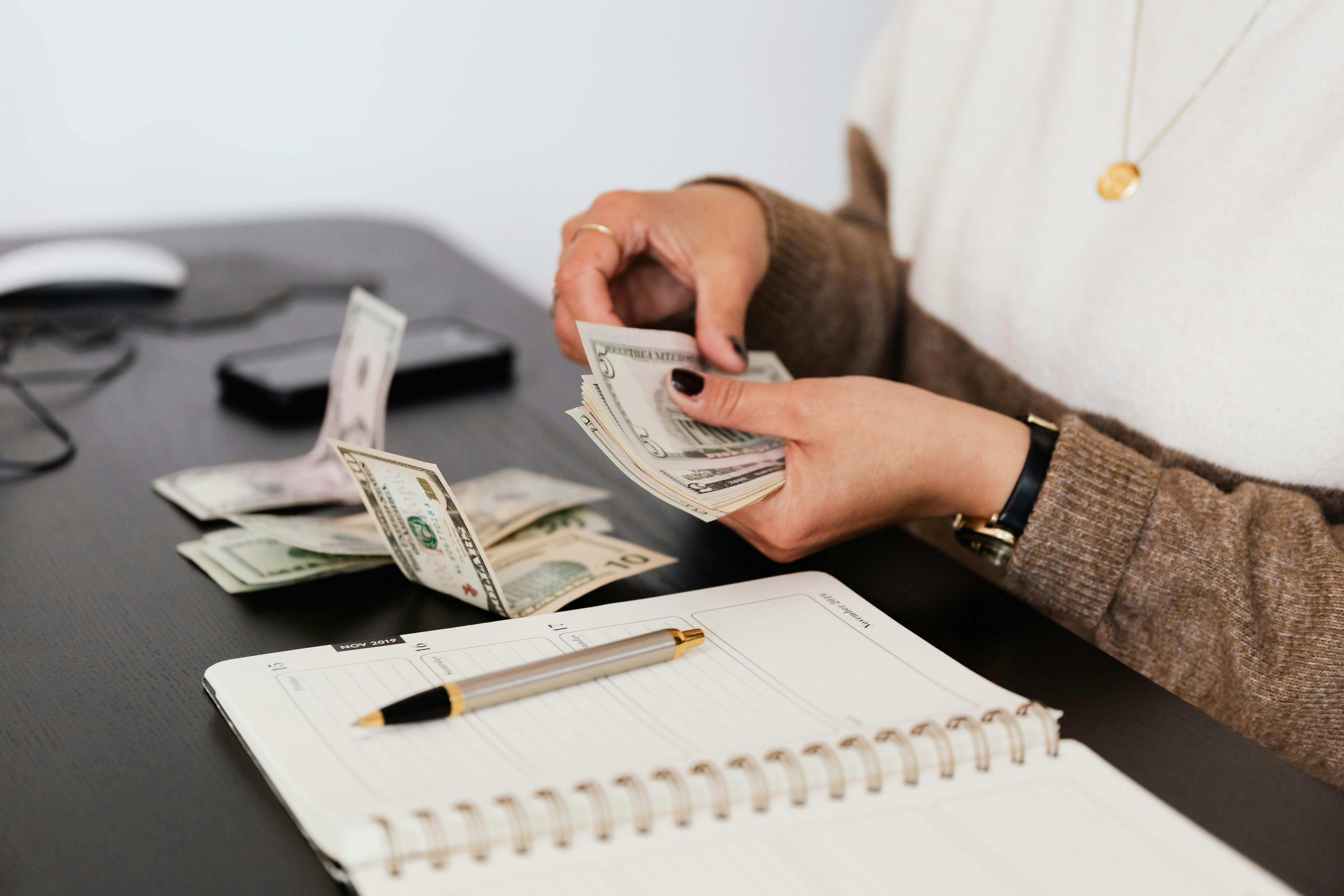 someone sitting at a desk counting cash with a pen and paper next to them